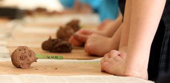 Highlanes Gallery Primary School Programme, Class Workshop, Spring 2022. children's hands pressing edge of table with clay heads on table