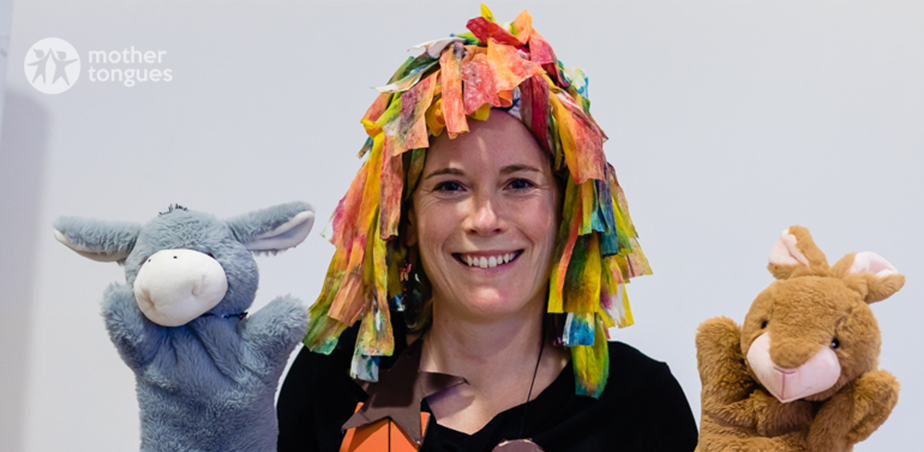 A woman wearing a multi-coloured wig holds two hand-puppets in each hand