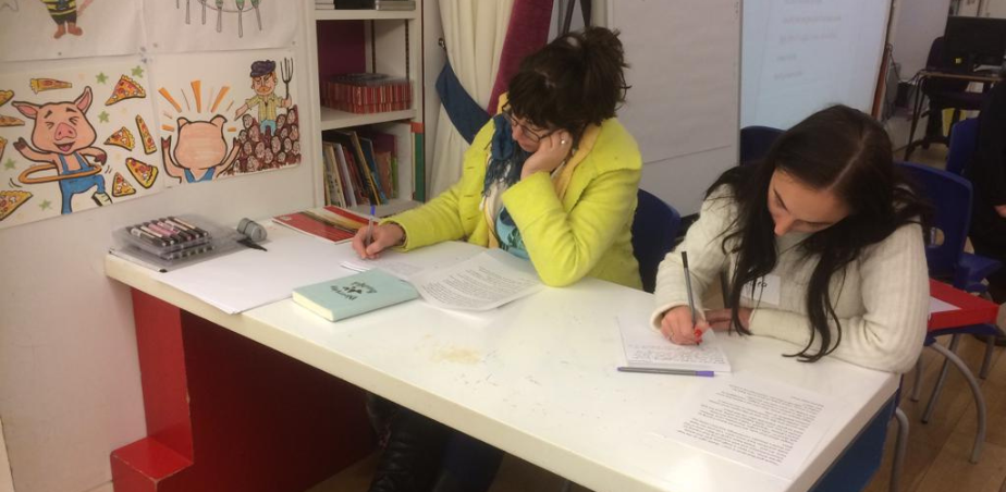 Two women sitting at a white table writing independently