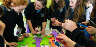 a group of teenage school children surround a table with colourful craft making materials