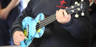 Close up of a primary school child playing a ukulele painted in hues of blue and yellow with splatter effect