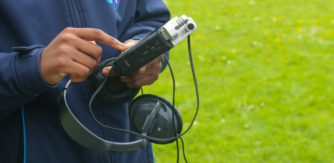 Close up of a student holding a digital audio recorder on location in a green area