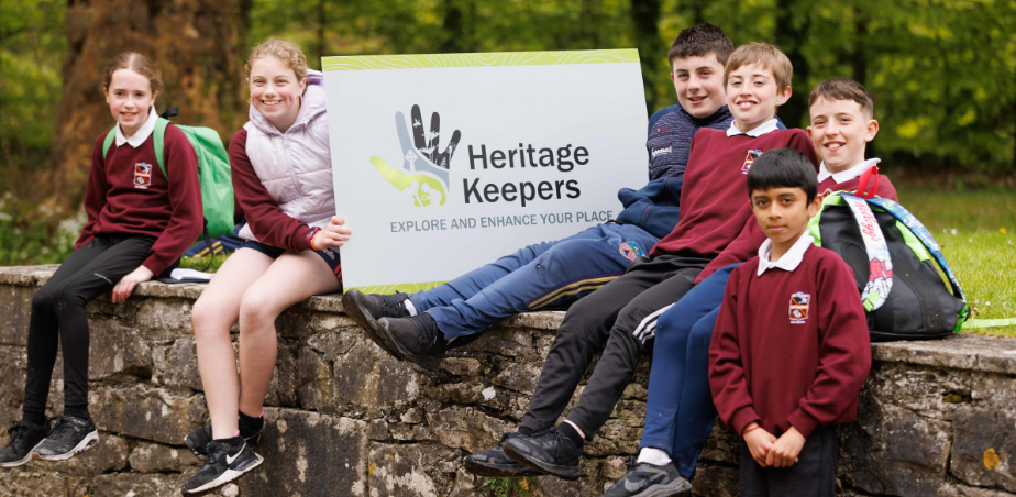 School children sitting on wall with heritage keeper sign