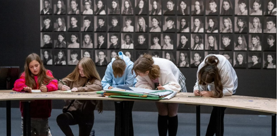 Children at desk in front of wall at portraits