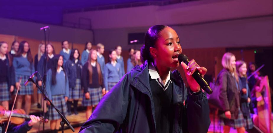 School student singing on stage in front of a choir for Waltons School of Music competition finalists 2024