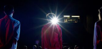 Cinema lens beam shines on the back of a boys head standing in a darkened cinema