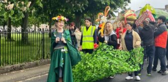 A group of students parade with large art props with a nature theme.