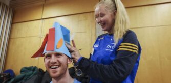 A DCU student places a colourful paper hat on another students head.