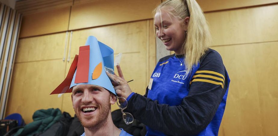 A DCU student places a colourful paper hat on another students head.