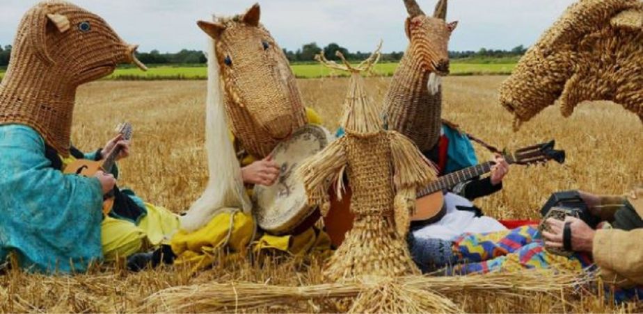 Musicians wearing straw weaved heads sit in a cut wheat field.