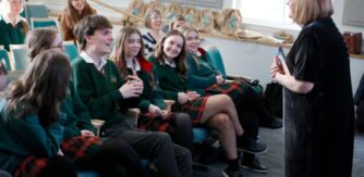 A group of students seated laughing with a Patricia Forde who stands speaking to them