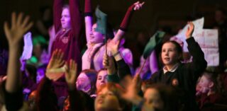 An audience of young people with raised hands and banners at a film awards event