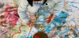 A child paints on a large white cloth covered in colourful swirls
