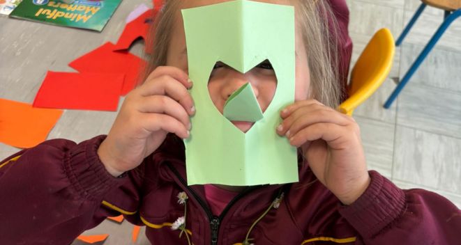 student holds a light green card with a love heart cut out in front of their face