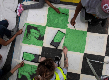 Young people painting green and white checkerboard pattern on the road for Open Road project